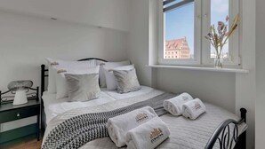 Ein Hotelzimmer mit einem Bett, Kissen, einem Nachttisch mit Lampe und einem Fenster mit Blick auf ein Gebäude.