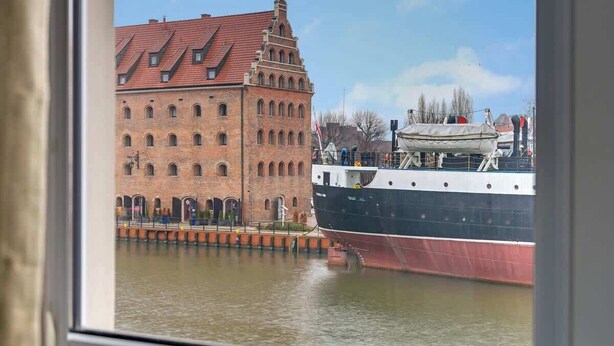 Ein großes Schiff liegt neben einem historischen Gebäude mit rotem Dach vor Anker.