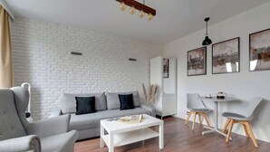 Ein modernes Wohnzimmer mit weißer Ziegelwand, grauem Sofa, weißem Couchtisch und einer kleinen Essecke mit Stühlen und Tisch.
