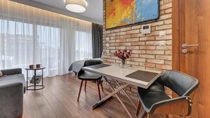Ein modernes Zimmer mit Esstisch, Stühlen, einer Couch, einem kleinen Beistelltisch und einem großen Fenster mit durchsichtigen Vorhängen.