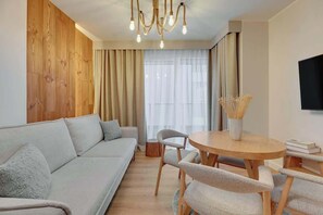 A modern living room with a sofa, round wooden table, chairs, and a TV mounted on the wall. - Merwede Residence 112 | by the Beach (Gdańsk)