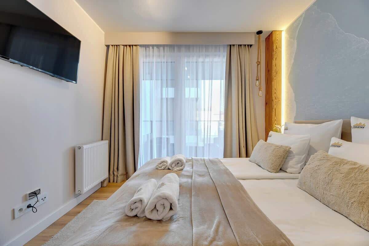 A hotel room with a bed, a TV mounted on the wall, a window with curtains, and a radiator.