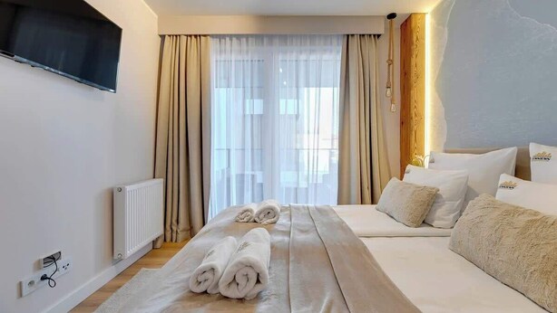 Een hotelkamer met een bed, een aan de muur bevestigde televisie, een raam met gordijnen en een radiator.