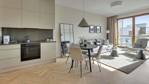 Ein modernes Wohnzimmer mit einer Couch, Sesseln, einem Esstisch und einer Küchenzeile mit Schränken und Geräten.