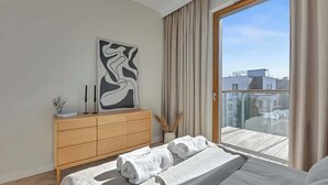 Ein modernes Schlafzimmer mit einem Bett, einer Holzkommode, einem großen abstrakten Gemälde und einem Balkon mit Blick auf die Stadt.