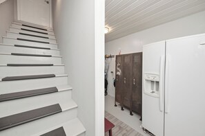 A staircase with handrails, a white refrigerator with a water dispenser, and a set of wooden lockers. - Sea Date Me: Ocean Views, Fenced Backyard (Oak Island)