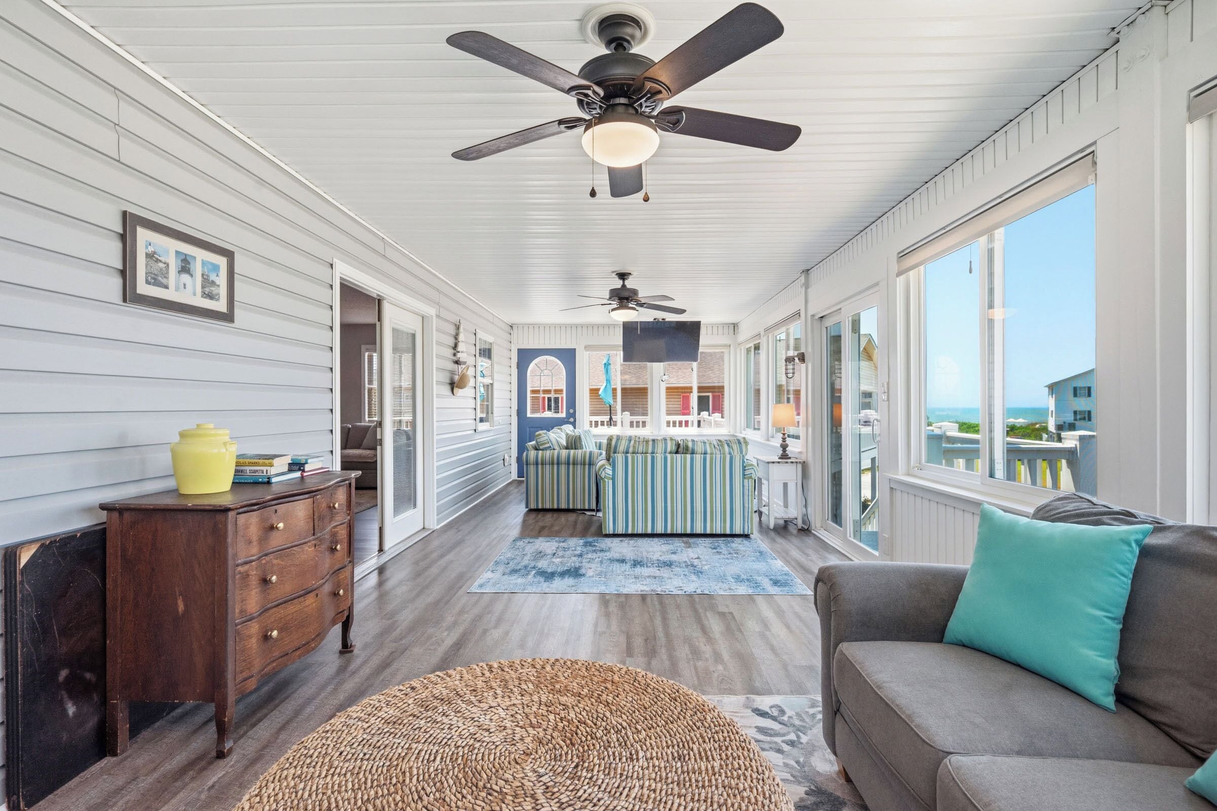 A room with a ceiling fan, a sofa, a loveseat, a wooden dresser, and a large window.
