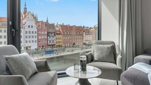 Ein modernes Hotelzimmer mit großem Fenster, zwei Sofas, einem kleinen Tisch und Blick auf eine Stadtansicht mit historischen Gebäuden.