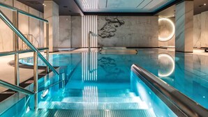 Ein moderner Innenpool mit Glastrennwand, einer Marmorwand mit Reliefbild und einer runden Leuchte.
