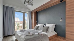 Ein modernes Schlafzimmer mit einem großen Bett, Blick auf Gebäude und einer Wand mit Holzverkleidung.