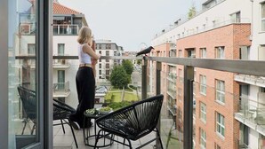 En balkon med udsigt over bybilledet, et bord med stole og en fugl på gelænderet.