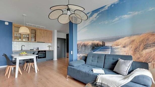 Un espacio habitable moderno con comedor, cocina y un gran mural de una escena de playa.