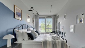 Un dormitorio moderno con cama, mesitas de noche, una lámpara y vistas al exterior.