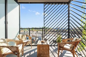 Een balkon met rieten meubels, een tafeltje en uitzicht op de stad.