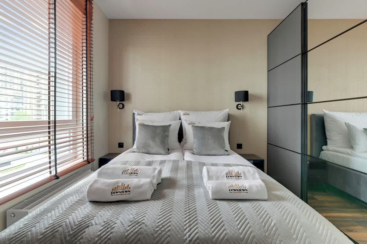 A hotel room with a large bed, two bedside tables, a wall-mounted lamp, and a window with blinds.