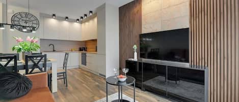 Una sala de estar moderna con televisor, una zona de comedor con sillas, un sofá y una mesita con un jarrón de flores.