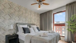 A bedroom with a bed, nightstand, lamp, and a view of a building through a window. - Nº 39 with Balcony | Pool, SPA & Gym (Gdańsk)