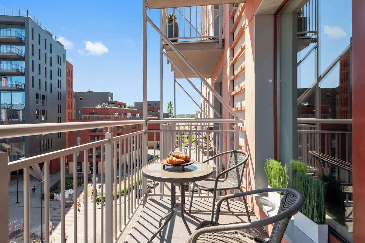 A balcony with a table and chairs, a potted plant, and a view of surrounding buildings.