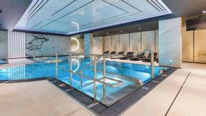 A modern indoor pool with clear glass walls, a sunken seating area, and a geometric ceiling design. - Deo Plaza 306 | View of the river and the Old Town (Gdańsk)