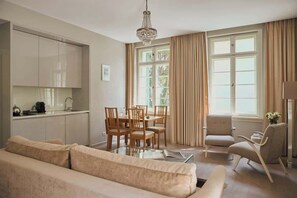 Ein Wohnzimmer mit einer Couch, einem Esstisch, Stühlen, einer Chandelüster und einem Fenster mit Vorhängen.