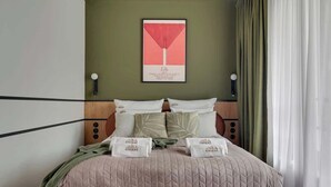 A neatly made bed with a quilted cover, pillows, and a blanket. There is a framed picture on the wall above the bed. - Doki G230 | Gdańsk Shipyard & Foodhall (Gdańsk)