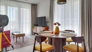A modern dining area with a round table, yellow chairs, and a television in the background. - Doki G230 | Gdańsk Shipyard & Foodhall (Gdańsk)