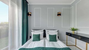 Quarto de hotel moderno com uma cama grande, duas mesas de cabeceira, uma escrivaninha e uma janela ampla com cortinas.
