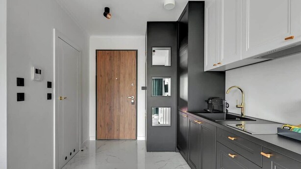 Cozinha moderna com piso de mármore, porta de madeira e armário preto com torneira dourada.