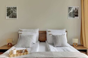 Un lit double avec une literie blanche, deux oreillers, une tête de lit en bois, une table de chevet avec une lampe et deux tableaux encadrés accrochés au mur.