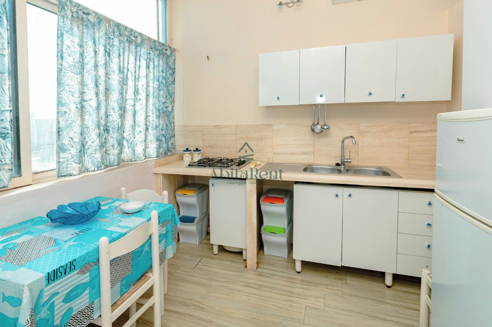 Une cuisine compacte équipée d’une cuisinière à gaz, d’un évier, de placards et d’une table recouverte d’une nappe bleue.