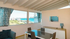 Ein Zimmer mit Glastisch, Stühlen, einer Couch, Meerblick, Deckenventilator und einem Gemälde.