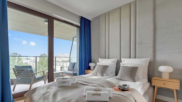 Een hotelkamer met een groot bed, een balkon met een stoel en uitzicht op de stad.