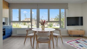 A modern living room with a round dining table, four chairs, a TV, and large windows with a view of buildings. - Żurawie B100B | Shipyard | Foodhall Montownia (Gdańsk)