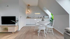 Un salon moderne doté d’un téléviseur à écran plat, d’une table à manger avec des chaises, d’un coin cuisine avec un pare-feu en marbre et d’un escalier.