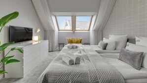 Une chambre moderne dotée d’une lucarne, d’un téléviseur à écran plat, d’une commode blanche et d’un grand lit recouvert d’une courtepointe matelassée.
