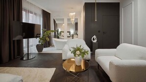 Ein stilvolles Wohnzimmer mit Flachbildfernseher, weißen Sofas, einem runden Couchtisch und einer Topfpflanze.