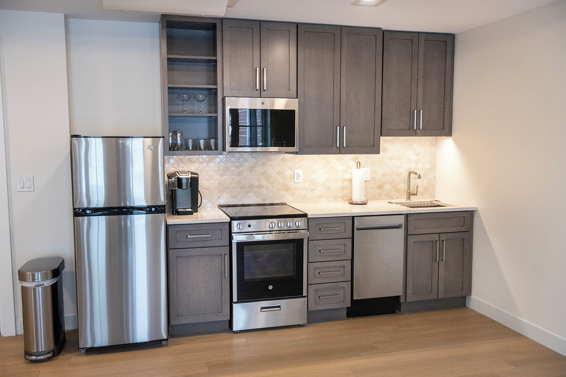 Una cocina moderna con electrodomésticos de acero inoxidable, armarios grises y piso de madera.