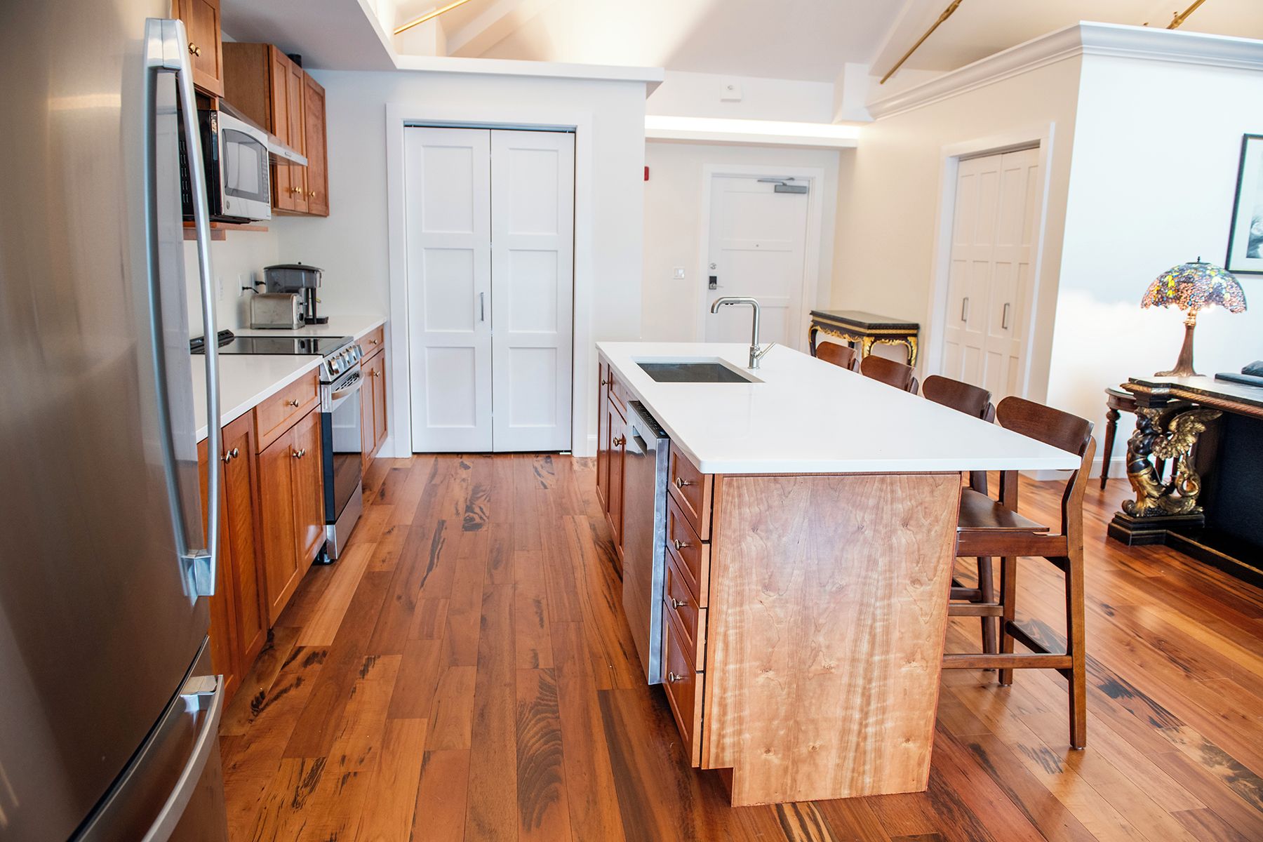 A modern kitchen with wooden cabinets, a built-in microwave, a stainless steel refrigerator, and a central island with seating.