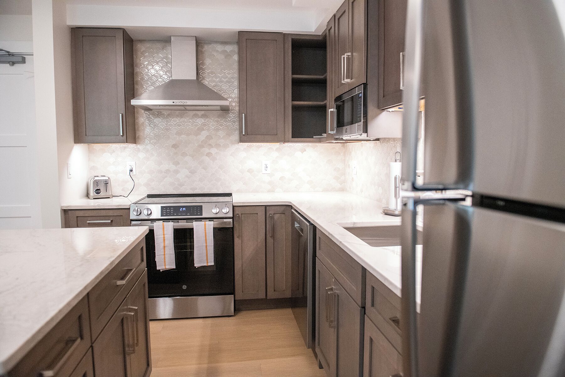 A modern kitchen with stainless steel appliances, wooden cabinets, and a tiled backsplash.