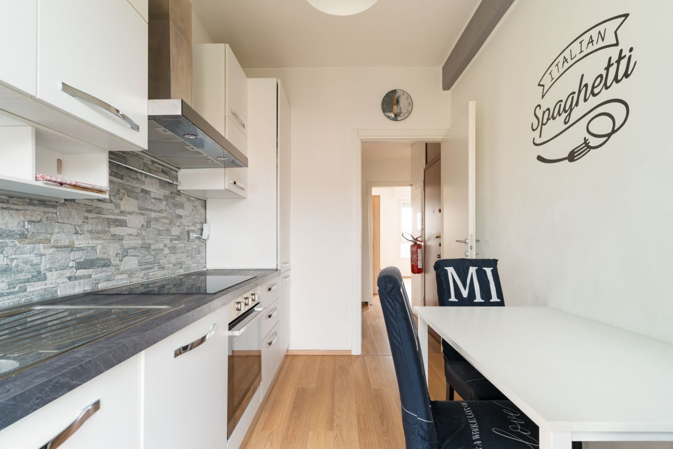 Een moderne keuken met witte kastjes, een betegelde achterwand en een eetgedeelte met een witte tafel en stoelen.