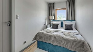 Ein Schlafzimmer mit Bett, Vorhängen, Fenster, Lampe und Tür.