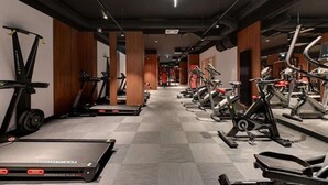 Ein Fitnessraum mit Laufbändern, Crosstrainern und Krafttrainingsgeräten, die in Reihen angeordnet sind.
