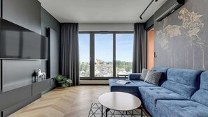 Ein modernes Wohnzimmer mit einem blauen Sofa, einem runden Couchtisch und einem großen Fenster mit Blick auf die Stadt.