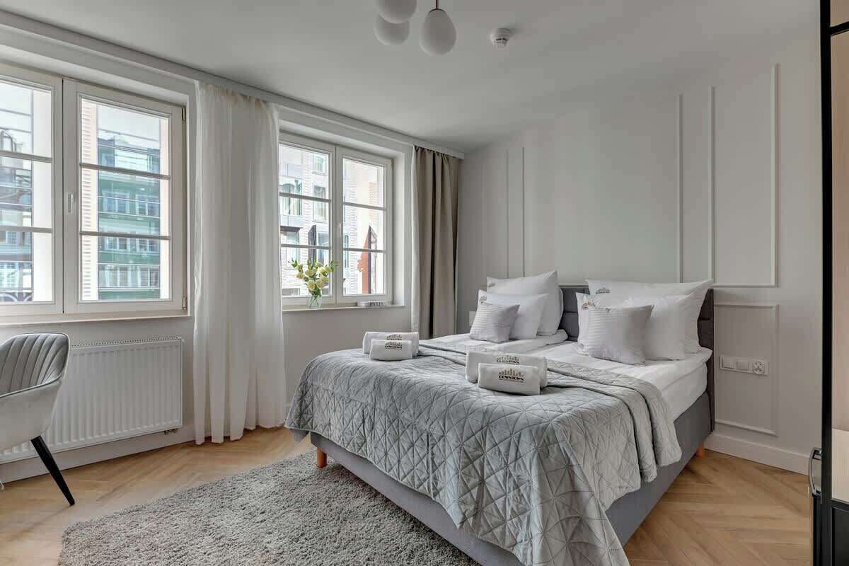 Ein modernes Schlafzimmer mit einem großen Bett, einem Fenster mit Vorhängen, einem Heizkörper und einem Sessel.