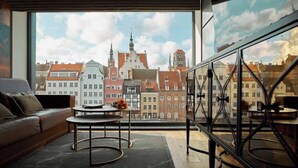 Et moderne interiør med et stort vindue der kigger ud over bybilledet, en lædersofa, et rundt bord og gelænder i glas.