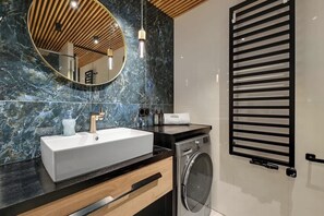 Une salle de bain moderne avec un pare-baignoire en marbre, un grand miroir, un lavabo, un lave-linge et un porte-serviettes.