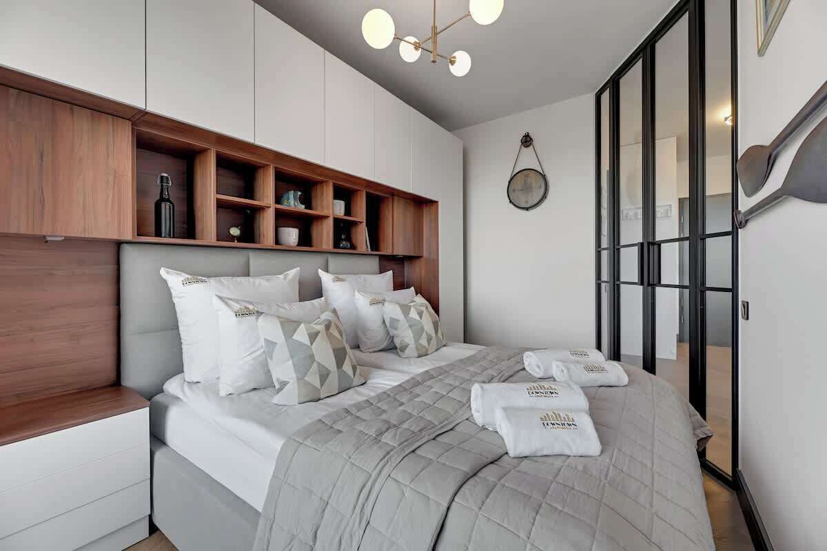 Une chambre d’hôtel moderne, dotée d’un lit, d’étagères en bois intégrées, d’un miroir rond et d’une porte coulissante en verre.