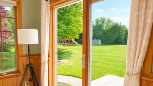 A room with a sliding glass door leading to a backyard with a lawn and a play structure.