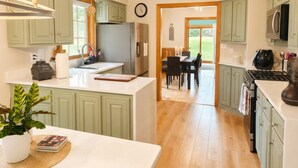 A kitchen with green cabinets, a refrigerator, a stove, and a dining area with a table and chairs.