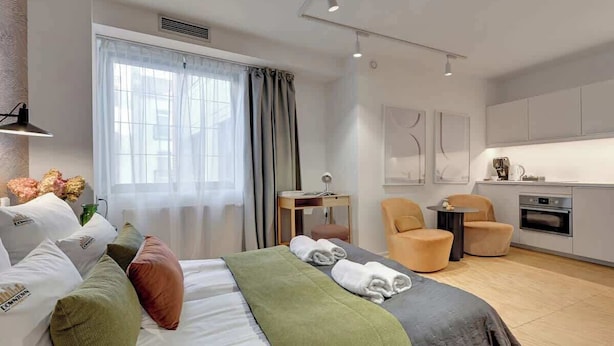 Ein modernes Hotelzimmer mit Bett, Schreibtisch, Stuhl, kleinem Tisch und einer Küchenzeile.